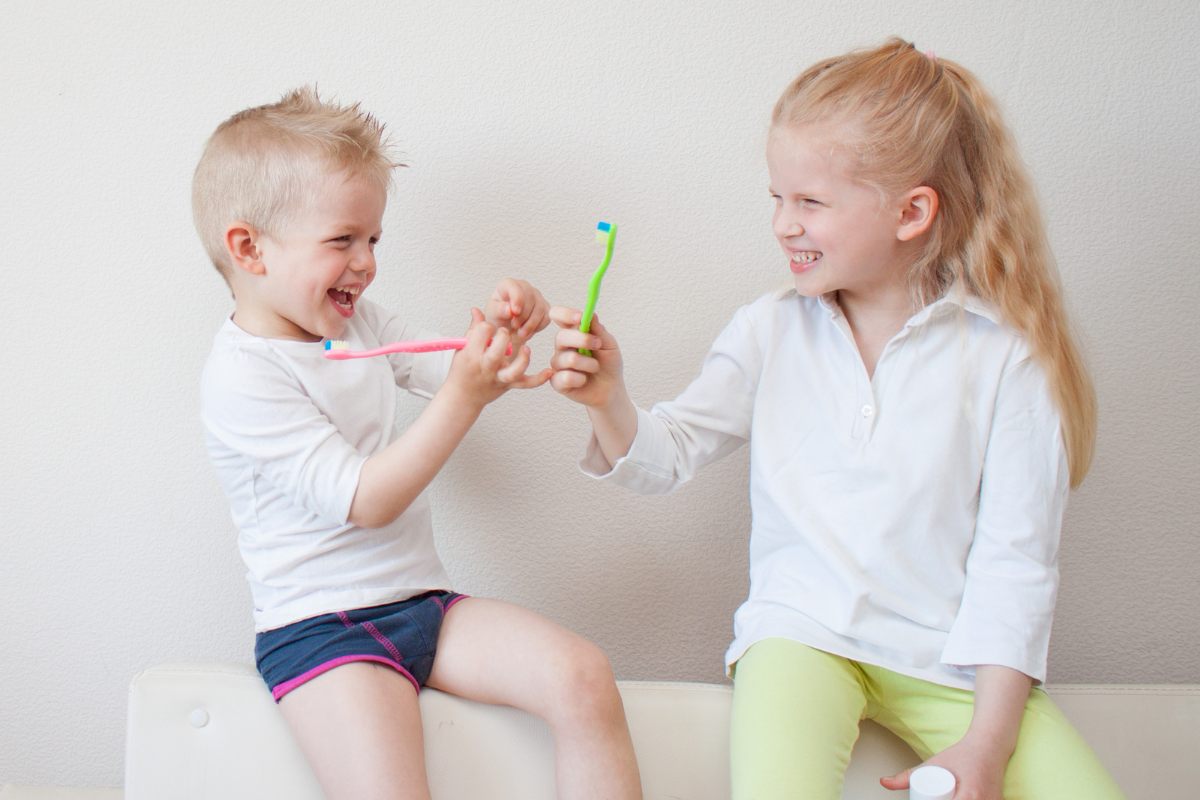 3 Things to Know Before the Tooth Fairy Visits Two young children playing with a green toy while sitting on a white surface indoors.