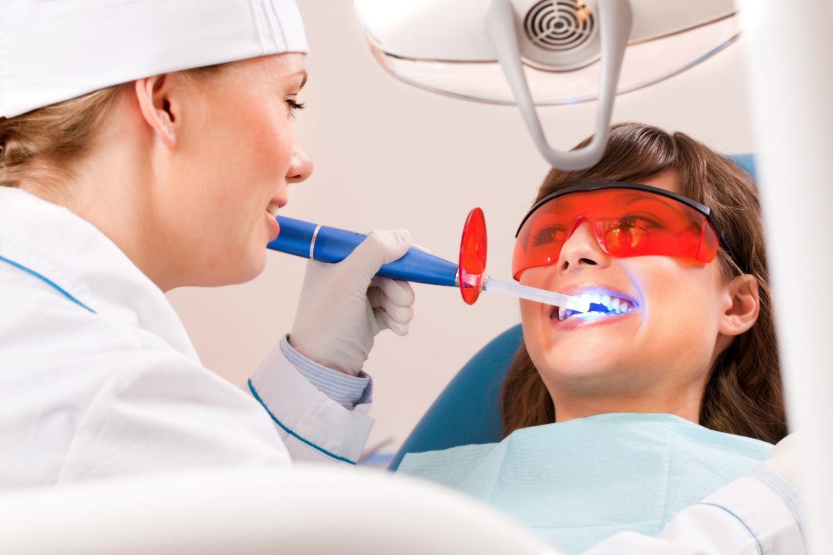 Pediatric dentist examining young patient's teeth using intraoral camera in dental office.