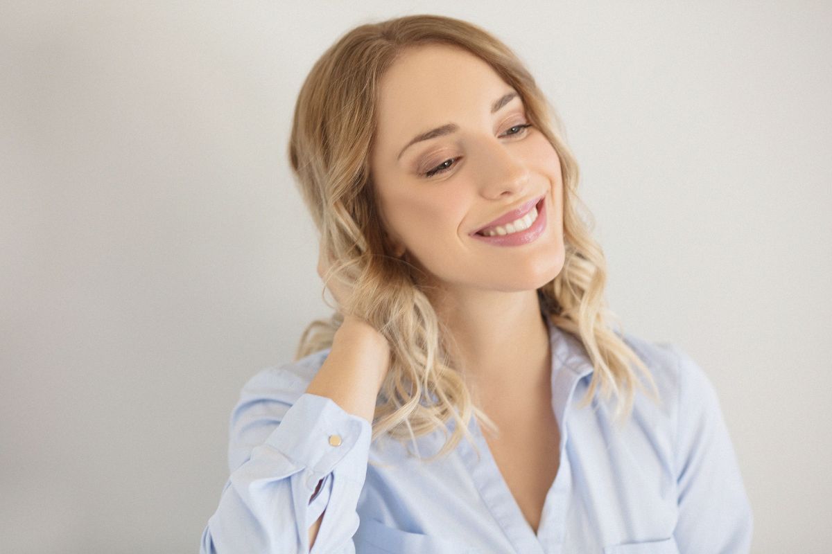 Do You Love to Smile Smiling woman with braided hair wearing light blue shirt against white background.